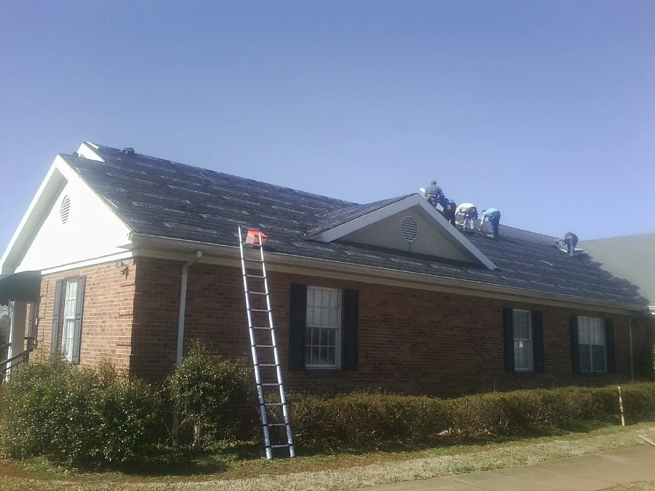 Crew tearing shingles off a brick ranch roof with a ladder set — Emergency Roof Repair work by our crew in Pricedale