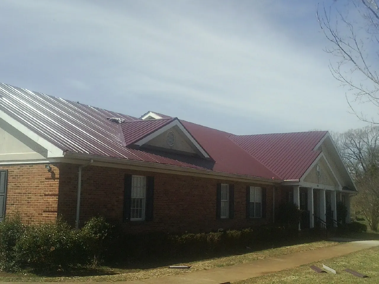 Red metal roof with gabled entries on a long brick building, from a Hail Damage Roof Repair job in Pricedale