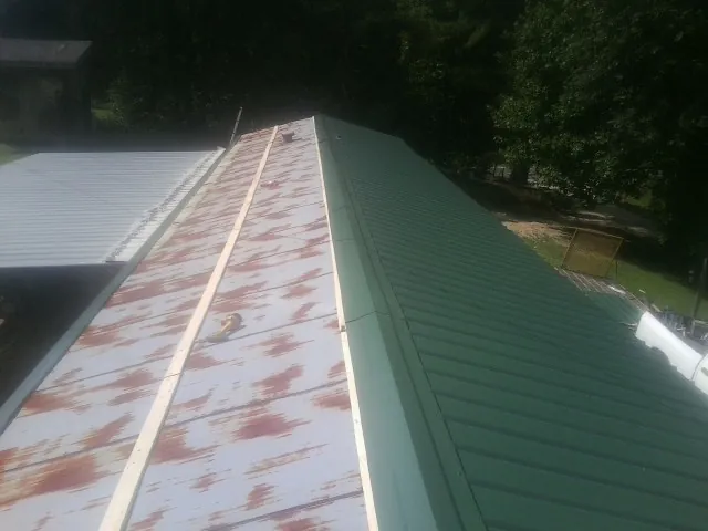Old rusted panels beside newly installed green metal roofing — Wind Damage Roof Repair by Roofing Brothers in Pricedale