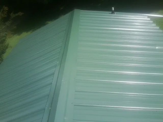 New green metal panels meeting at the ridge of a roof — Flat Roof Repair work by our crew in Pricedale