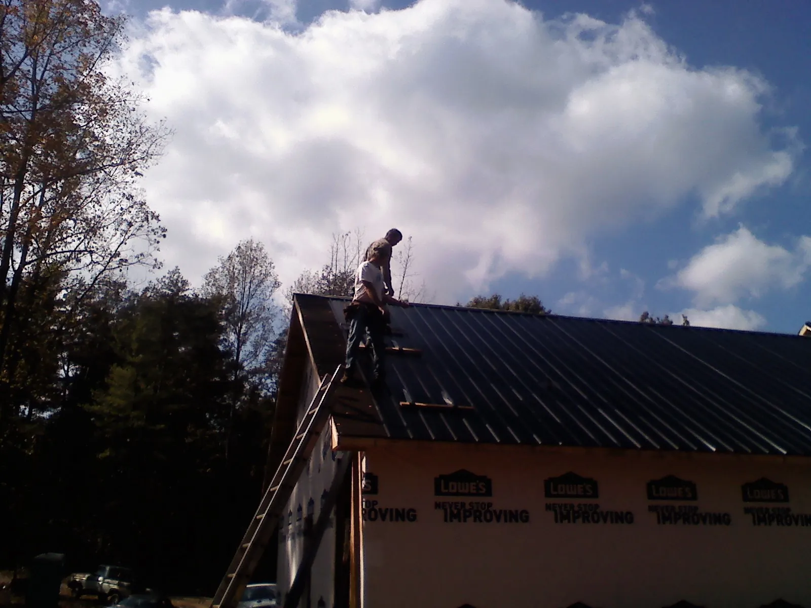 Roofer fastening dark metal panels high against a cloudy sky, from a Roof Inspection job in Pricedale