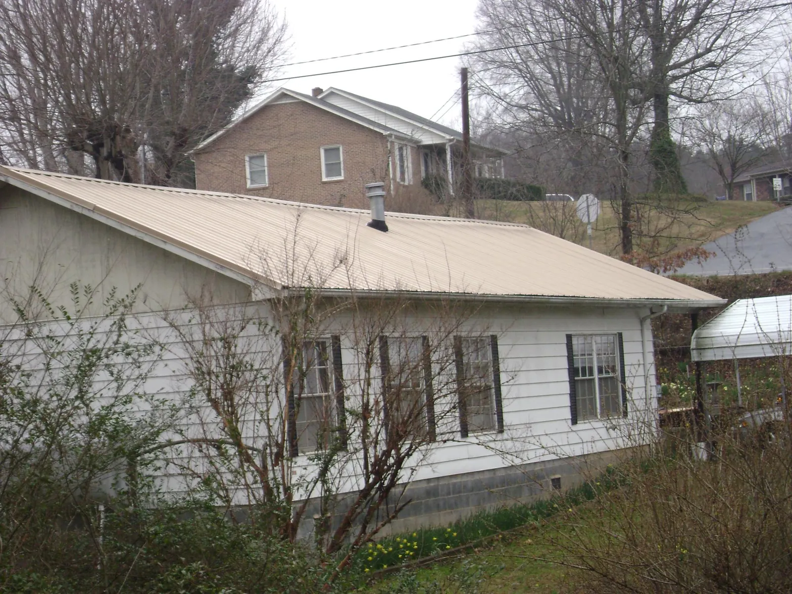 Tan metal roof on a white sided house set into a hillside — Commercial Roofing by Roofing Brothers in Pricedale