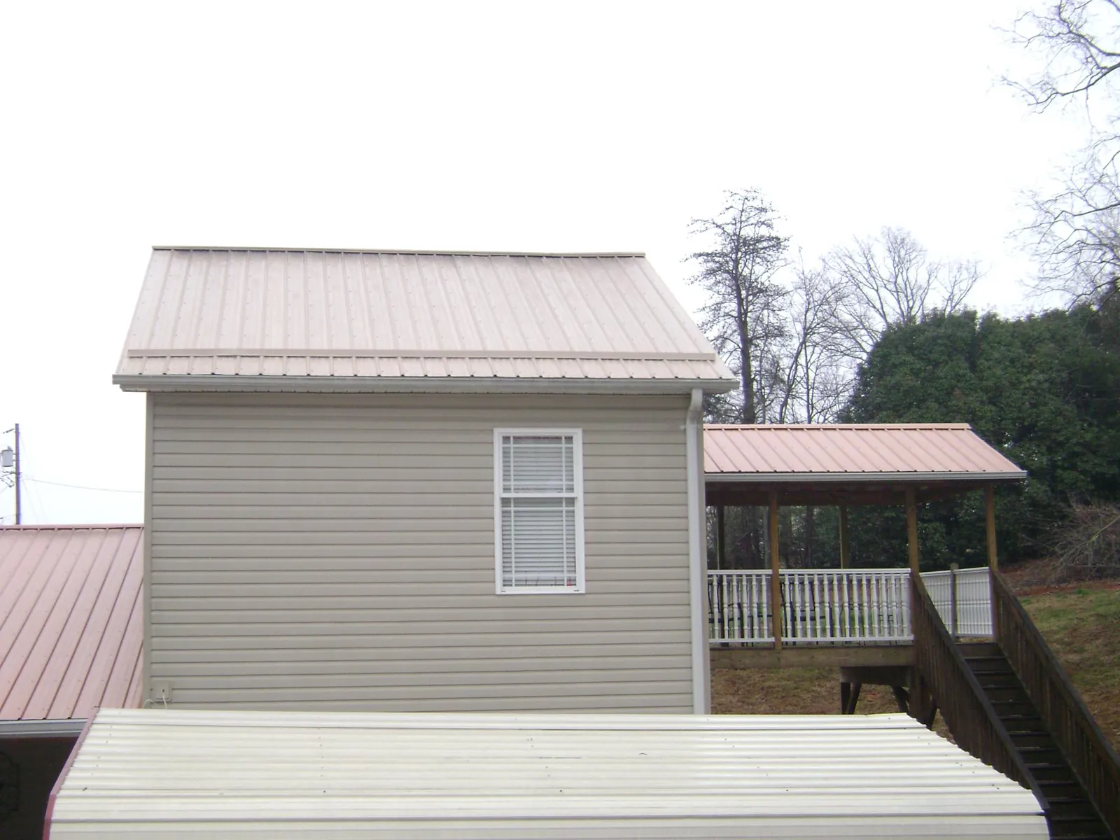 Tan metal roofs on a two story addition and attached porch, from a Roof Replacement job in Pricedale